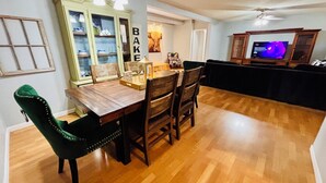 A dining area with a wooden table and chairs, a cabinet with glass doors, and a television in the background.
