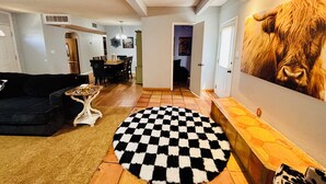 A living room with a black and white checkered rug, a dining area with a table and chairs, and a large wall painting of a cow's face.
