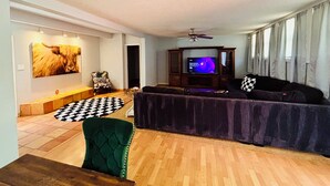 A living room with a sofa, a television, a ceiling fan, and a wall-mounted picture.