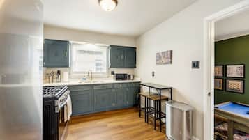 A compact kitchen with a gas stove, a sink, and a microwave. There is a small refrigerator and a table with two chairs. The kitchen has dark blue cabinets and a window above the sink.