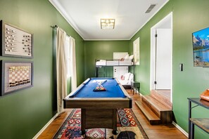 Una habitación con mesa de billar, literas y un tablero de ajedrez enmarcado.