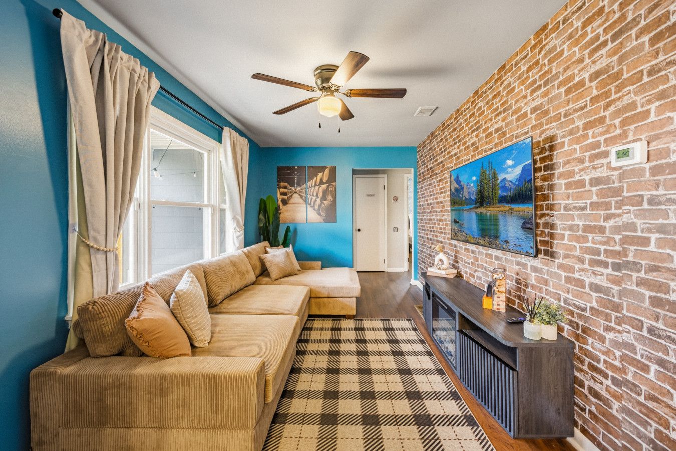 A living room with a sofa, a ceiling fan, a fireplace, and a brick wall.