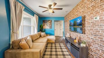 A living room with a sofa, a ceiling fan, a fireplace, and a brick wall.