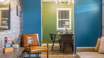 A room with a brick wall, a brown leather chair, a dining table with chairs, and a green wall.
