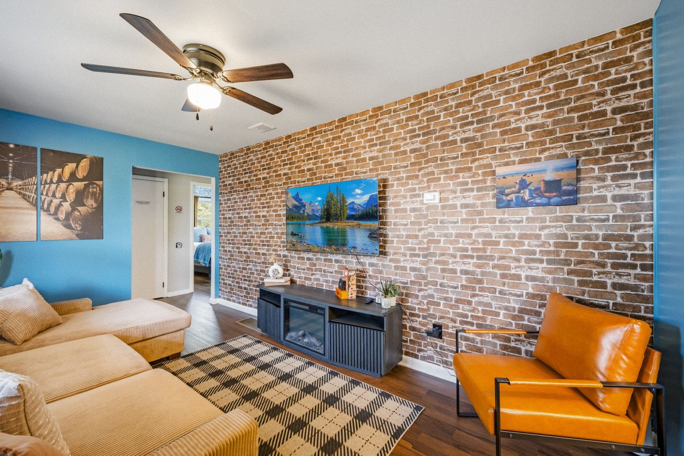 Ein Wohnzimmer mit Backsteinwand, Deckenventilator, Sofa, orangefarbenem Sessel und einem Gemälde.