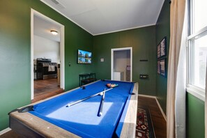 A pool table in a room with green walls, a wooden floor, and a window.