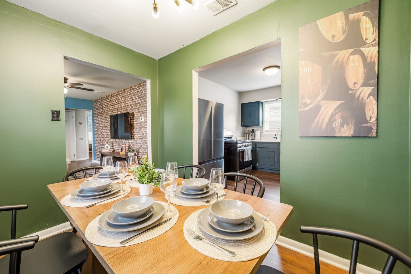 A dining area with a wooden table set for four, a brick wall, and a kitchen in the background.