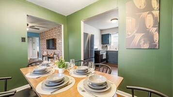 A dining area with a wooden table set for four, a brick wall, and a kitchen in the background.