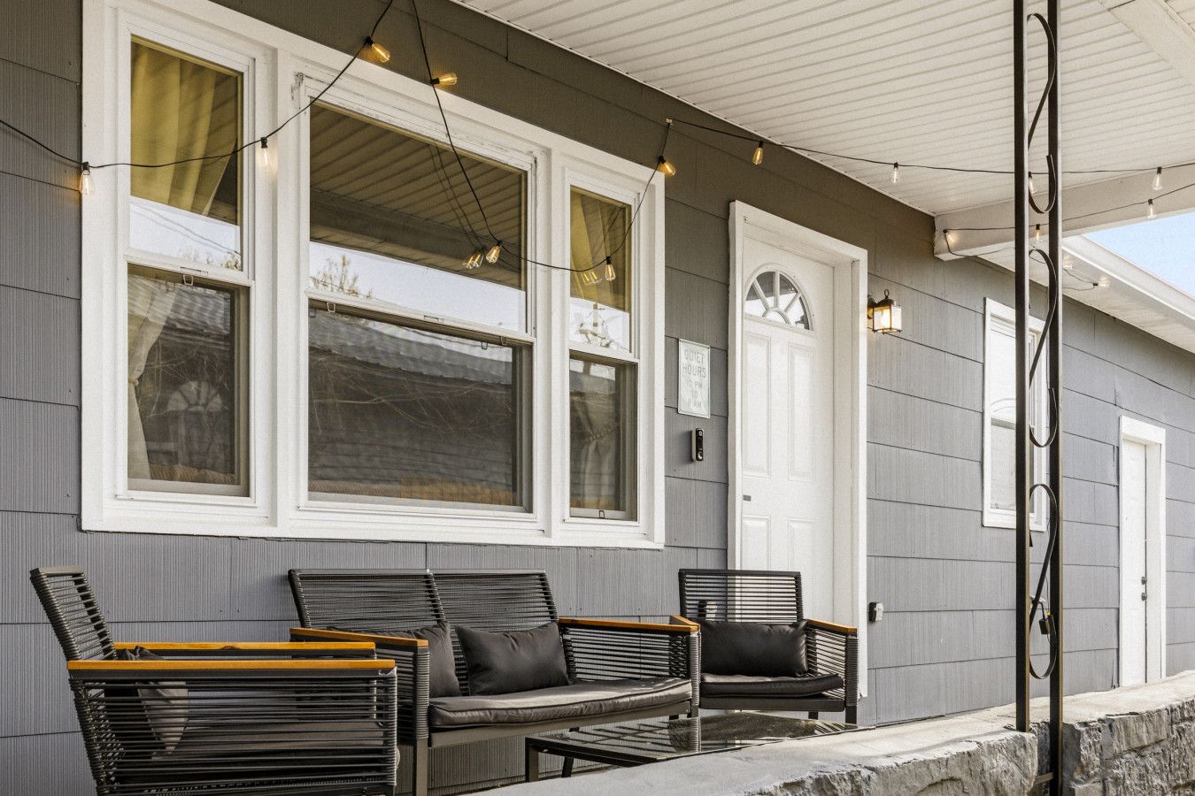A building with a porch, two chairs, and string lights.
