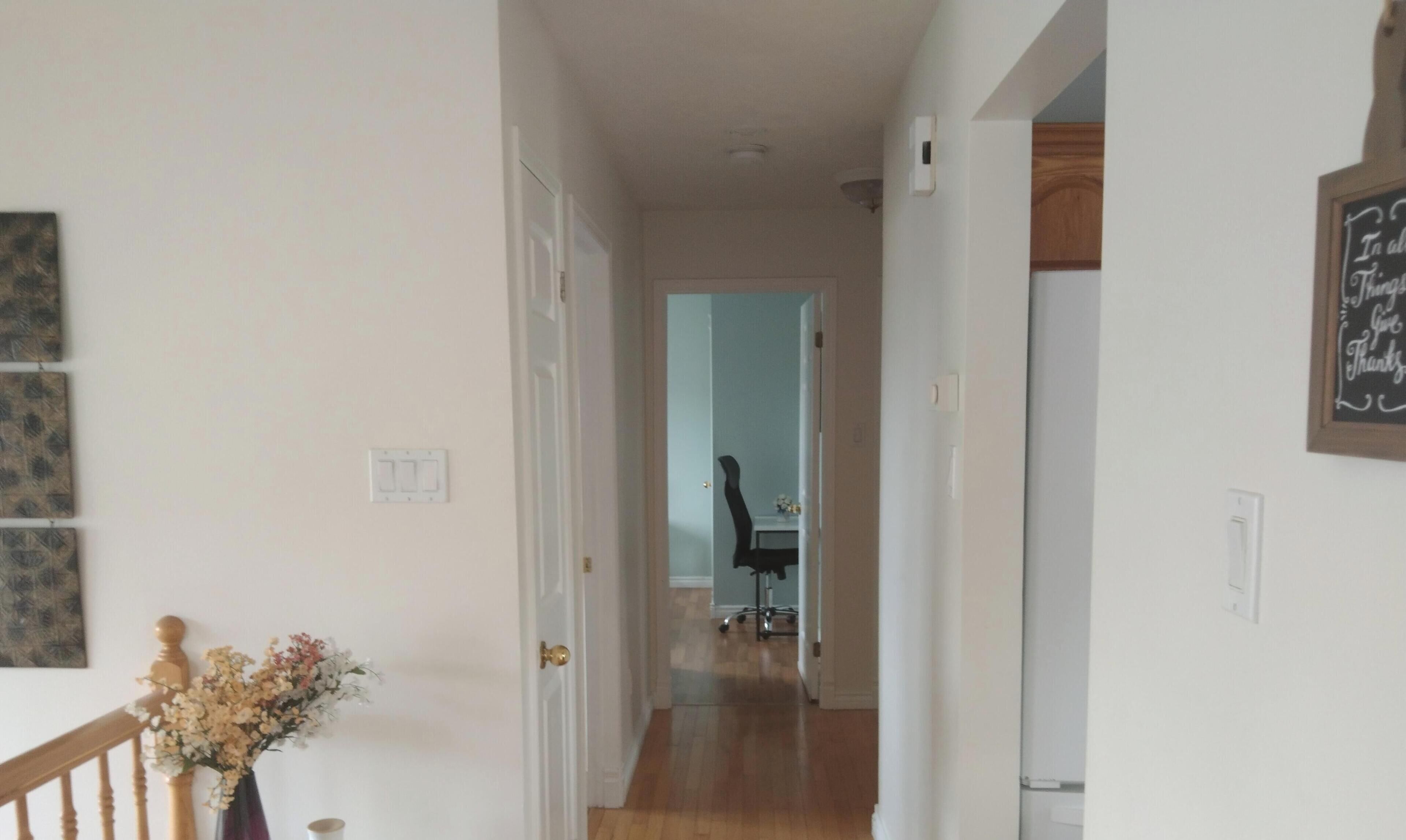 Un couloir avec un escalier en bois, une porte donnant sur une pièce et un panneau fixé au mur.