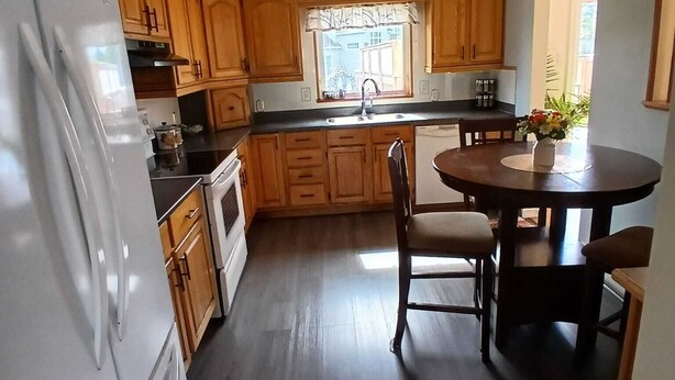 A kitchen with wooden cabinets, a white refrigerator, a dining table with chairs, and a window with a view.
