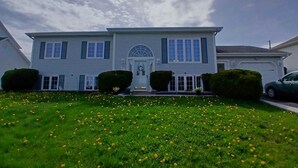 A two-story house with a front door, windows, and a lawn with yellow flowers.