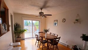 A dining area with a wooden table and chairs, a ceiling fan, and a view through a glass door to an outdoor patio.