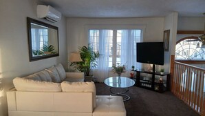 A living room with a white sofa, a glass coffee table, a TV, and a balcony with a railing.