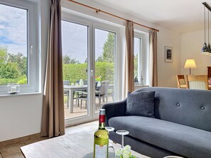 Een moderne woonkamer met een grijze bank, een eettafel met stoelen en een groot raam met gordijnen.