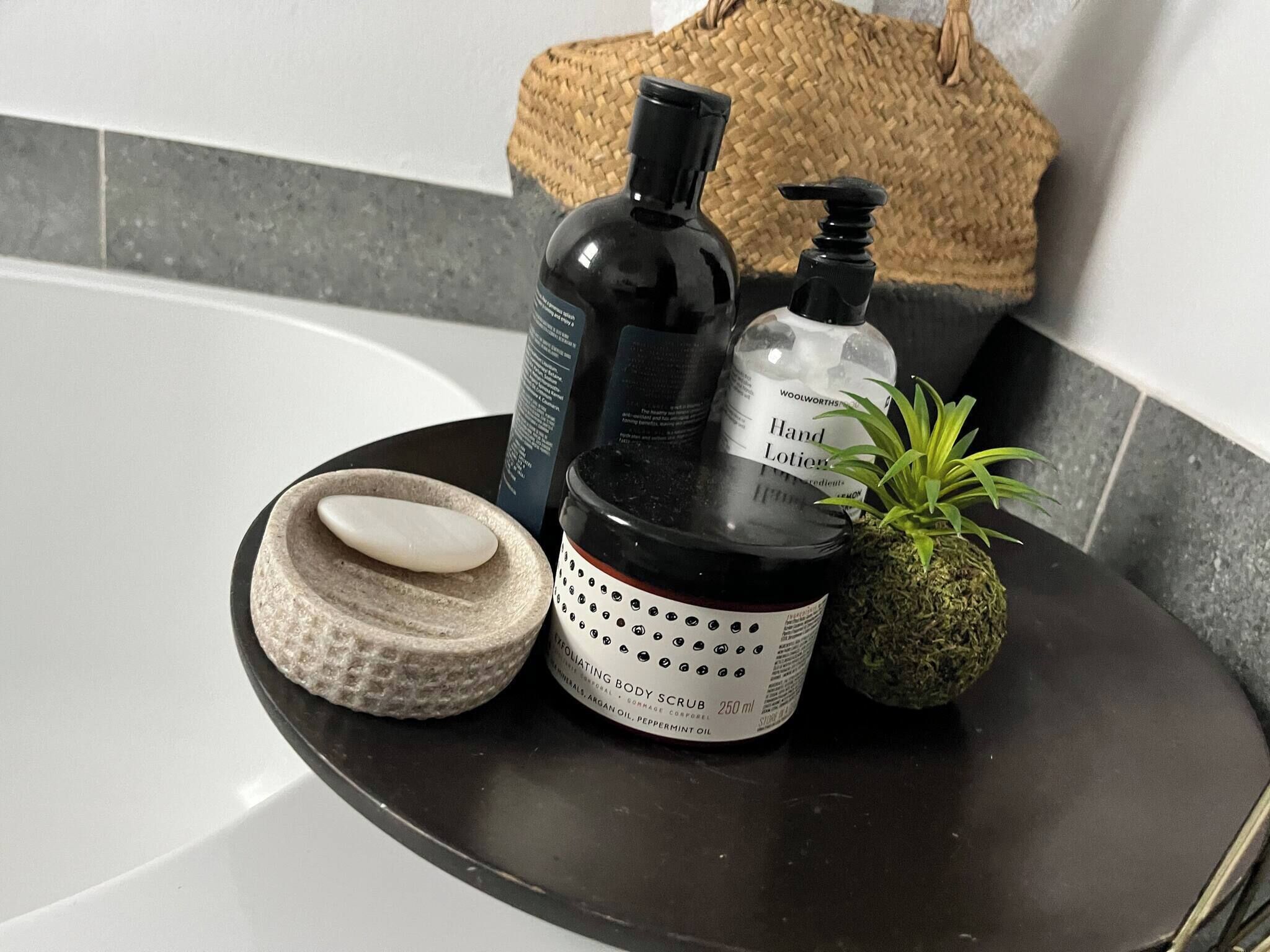 Un meuble-lavabo de salle de bain avec un plan de toilette noir, un porte-savon, un flacon de lotion pour les mains, un flacon de gommage pour le corps et une petite plante en pot.