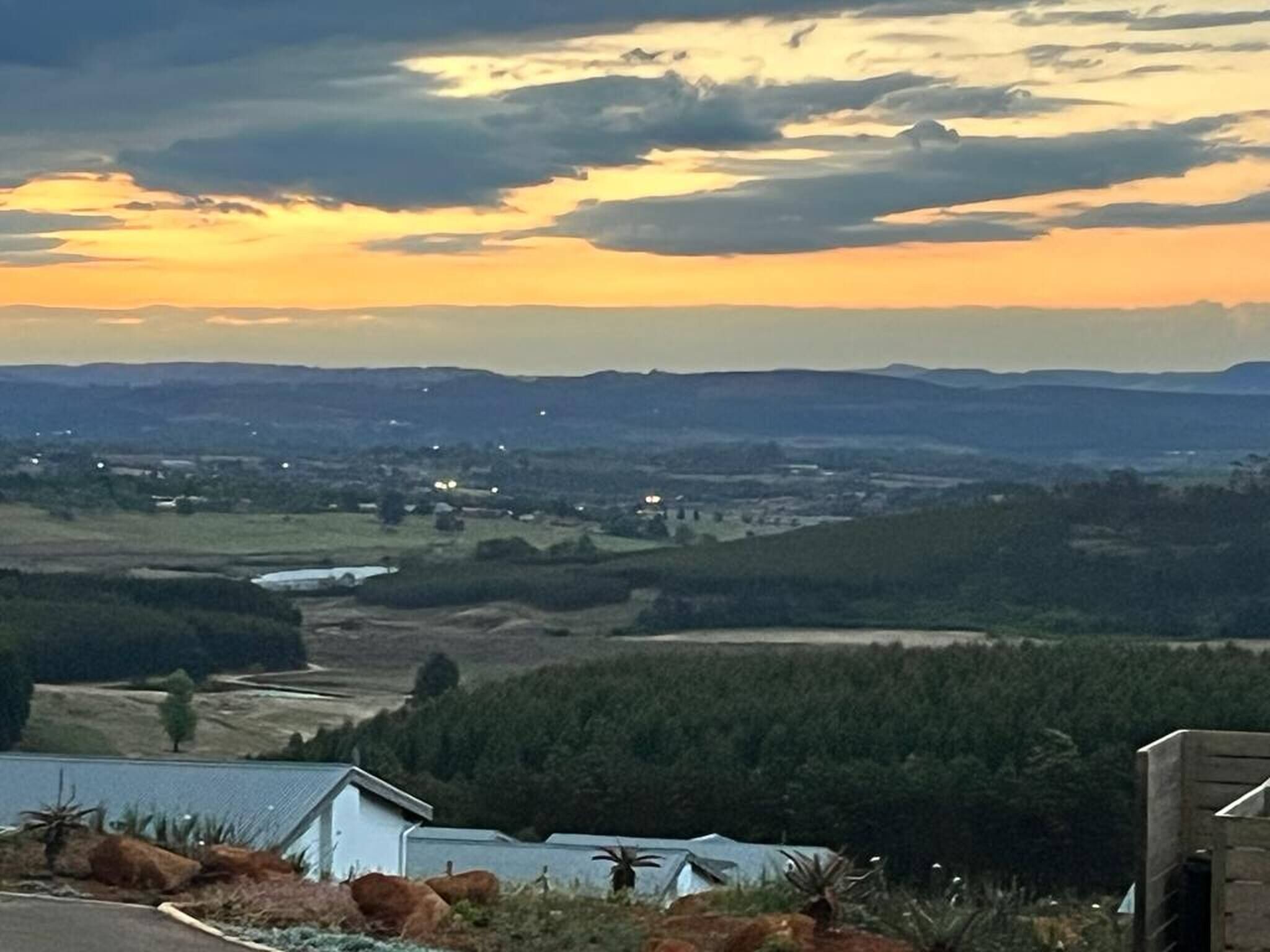 Un paisaje rural con una casa y una edificación pequeña al frente, rodeado de árboles y campos abiertos.