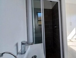 Un baño con mampara de vidrio, un lavabo blanco y paredes cubiertas de azulejos oscuros.