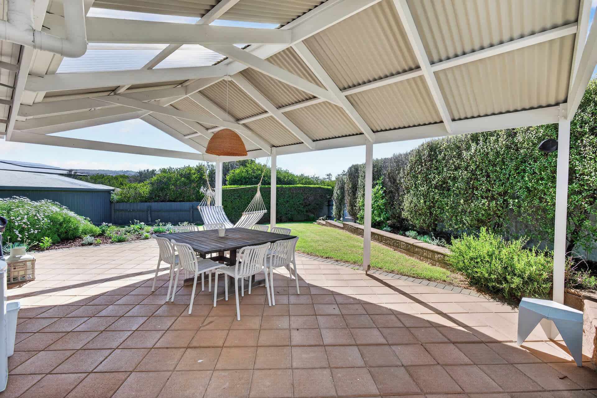 Un patio cubierto con una mesa y sillas, rodeado de un jardín.