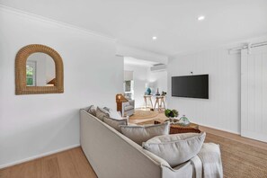 A living room with a sofa, a mirror, a television, and a door. - 6 England Avenue, Port Elliot (Port Elliot)