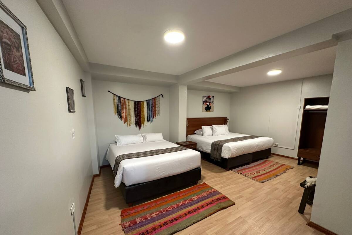 A hotel room with two beds, a wooden floor, and a colorful rug.