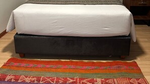 A neatly made bed with white linens, a colorful woven rug, and a wall hanging with multicolored tassels. - Hotel Boutique Qorikallpa (Cusco)