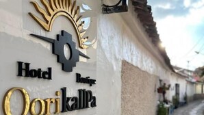A hotel sign with a sun design, the name 'Hotel Boutique Qorikalpa,' and a cobblestone street with potted plants. - Hotel Boutique Qorikallpa (Cusco)