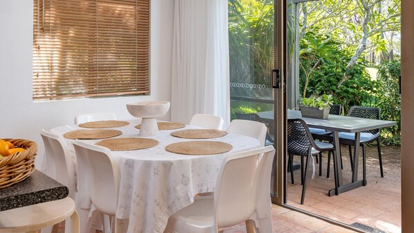 Un coin repas avec une table ronde, des chaises blanches et des sets de table en fibres tressées.