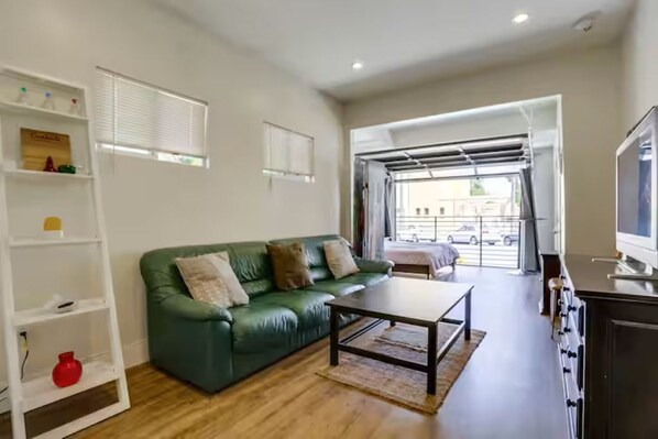 Un salón con un sofá verde, una mesa de centro, un televisor y una zona de cocina con estufa.