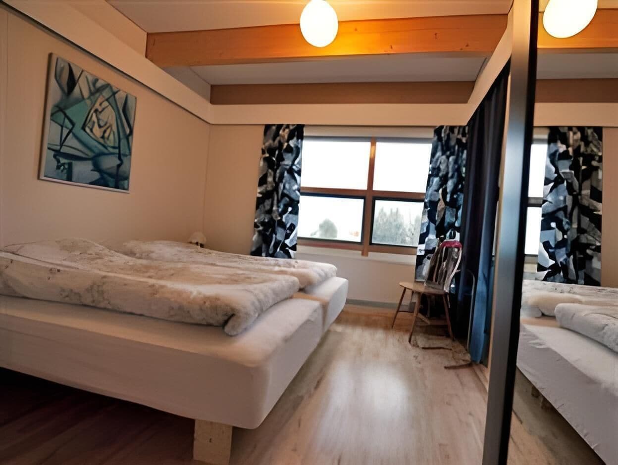 A room with two beds, a desk, a chair, a window with curtains, and a painting on the wall.