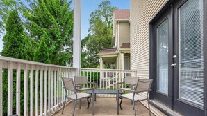 A balcony with a table and chairs, a white fence, and a building with a dark door and windows. - Big Group Getaway Near OSU with 6BR, 8 Beds, 5-Car Parking (Columbus)