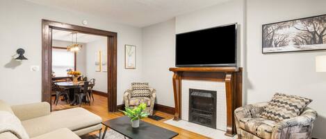 A living room with a fireplace, a flat-screen TV, and a dining area with a table and chairs.