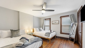 A hotel room with two beds, a ceiling fan, a flat-screen TV, and a wooden floor.