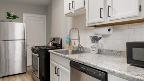 A modern kitchen with stainless steel appliances, white cabinetry, a granite countertop, and a built-in dishwasher.