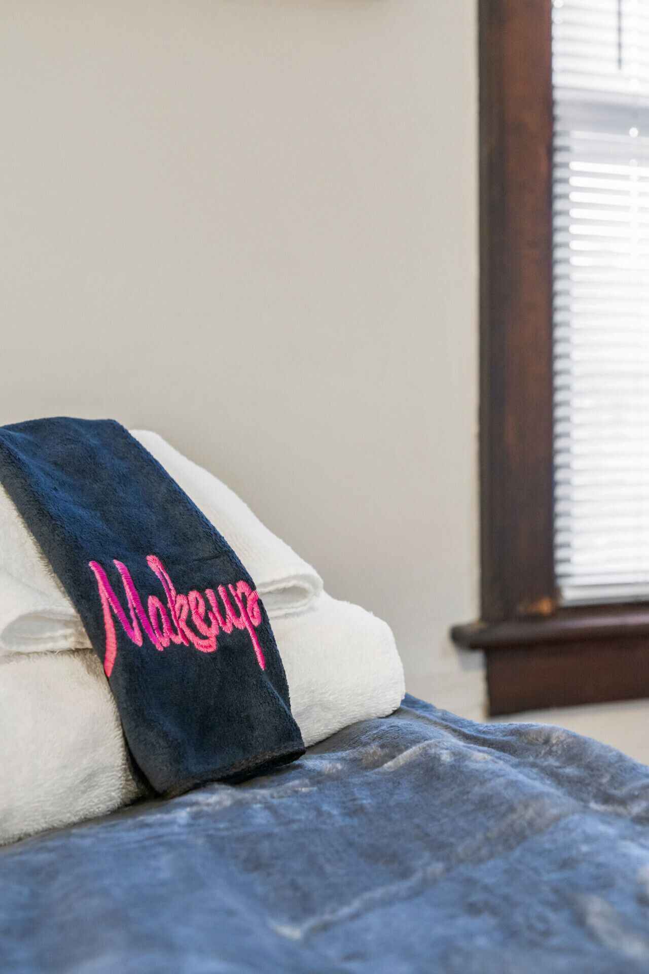 A neatly folded white towel with a dark blue towel on top, both with a pink embroidered text.