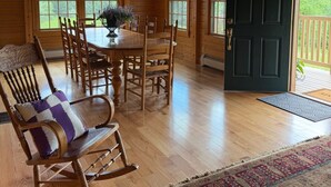 Un interior de madera con una mesa de comedor, sillas, un sillón mecedora y una puerta que da al exterior.