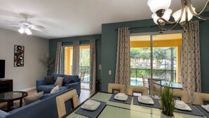 Un salon moderne avec un canapé, une table à manger pour quatre personnes et un balcon offrant une vue sur la piscine.