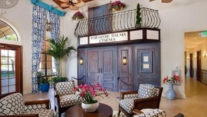 Un hall d’entrée avec des meubles aux motifs originaux, un balcon orné de plantes suspendues et une enseigne indiquant « Paradise Palms Cinema ».