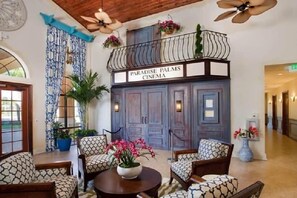 A lobby with patterned furniture, a balcony with hanging plants, and a sign reading 'Paradise Palms Cinema.' - Paradise Palm Home Stay (Kissimmee)