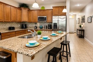 A kitchen with granite countertops, wooden cabinets, stainless steel appliances, and a central island with bar stools. - Paradise Palm Home Stay / Near parks (Kissimmee)