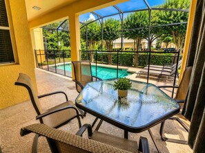 A glass-top table with chairs and a potted plant, overlooking a swimming pool and greenery. - Paradise Palm Home Stay / Near parks (Kissimmee)