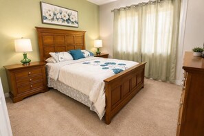 A bedroom with a wooden bed, two nightstands, a green vase, a floral painting, and a window with curtains. - Paradise Palm Home Stay / Near parks (Kissimmee)