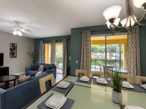 A modern living room with a sofa, dining table set for four, and a balcony with curtains. - Paradise Palm Home Stay / Near parks (Kissimmee)