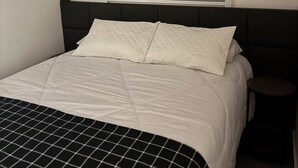 A bed with a black and white checkered bedspread, a white pillow, and a headboard. - Casa Vertice – Copacabana (Uberlândia)