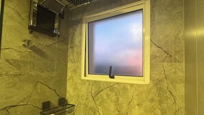 A bathroom with a shower, a window, and a marble wall. - Casa Vertice – Copacabana (Uberlândia)