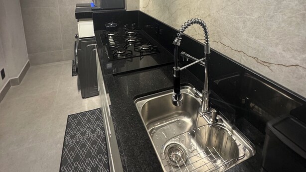 A modern kitchen with a black countertop, stainless steel sink, and a gas stove. - Casa Vertice – Copacabana (Uberlândia)