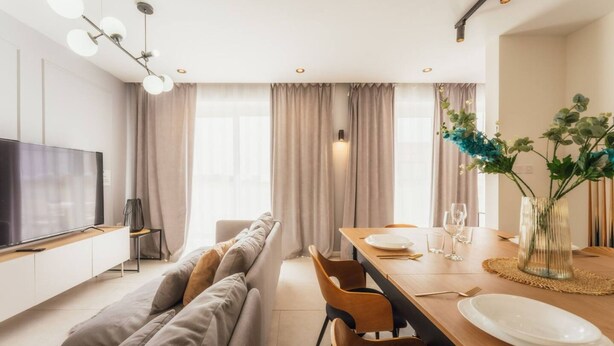 A modern living room with a sofa, a dining table set for two, and a TV on a cabinet. - Luxury Penthouse Jacuzzi BBQ Terrace Pool Table (Xaghra)