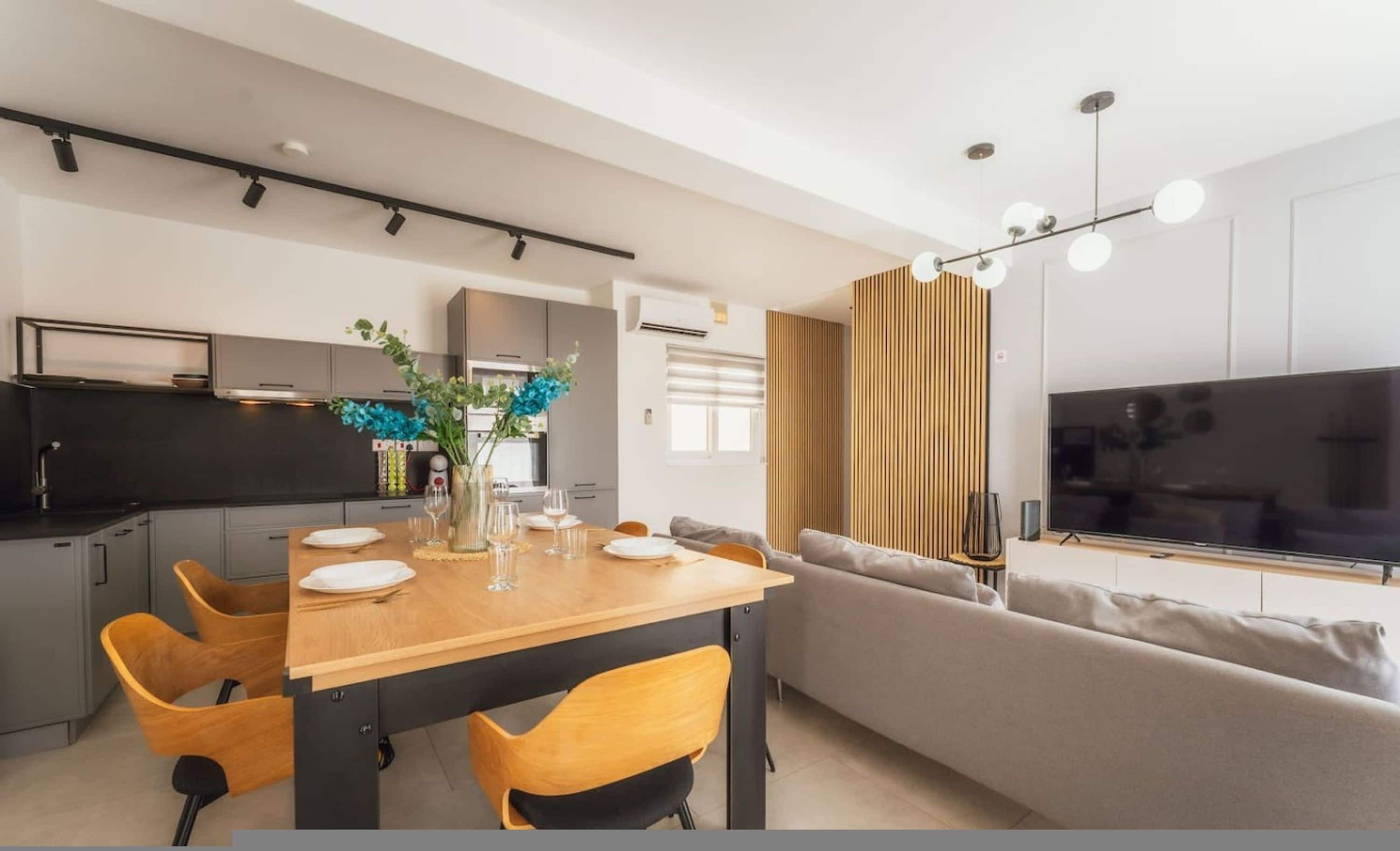 A modern kitchen with a dining area, a sofa, and a TV.