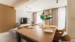 A modern dining area with a wooden table, chairs, a TV, and a decorative plant. - Luxury Penthouse Jacuzzi BBQ Terrace Pool Table (Xaghra)