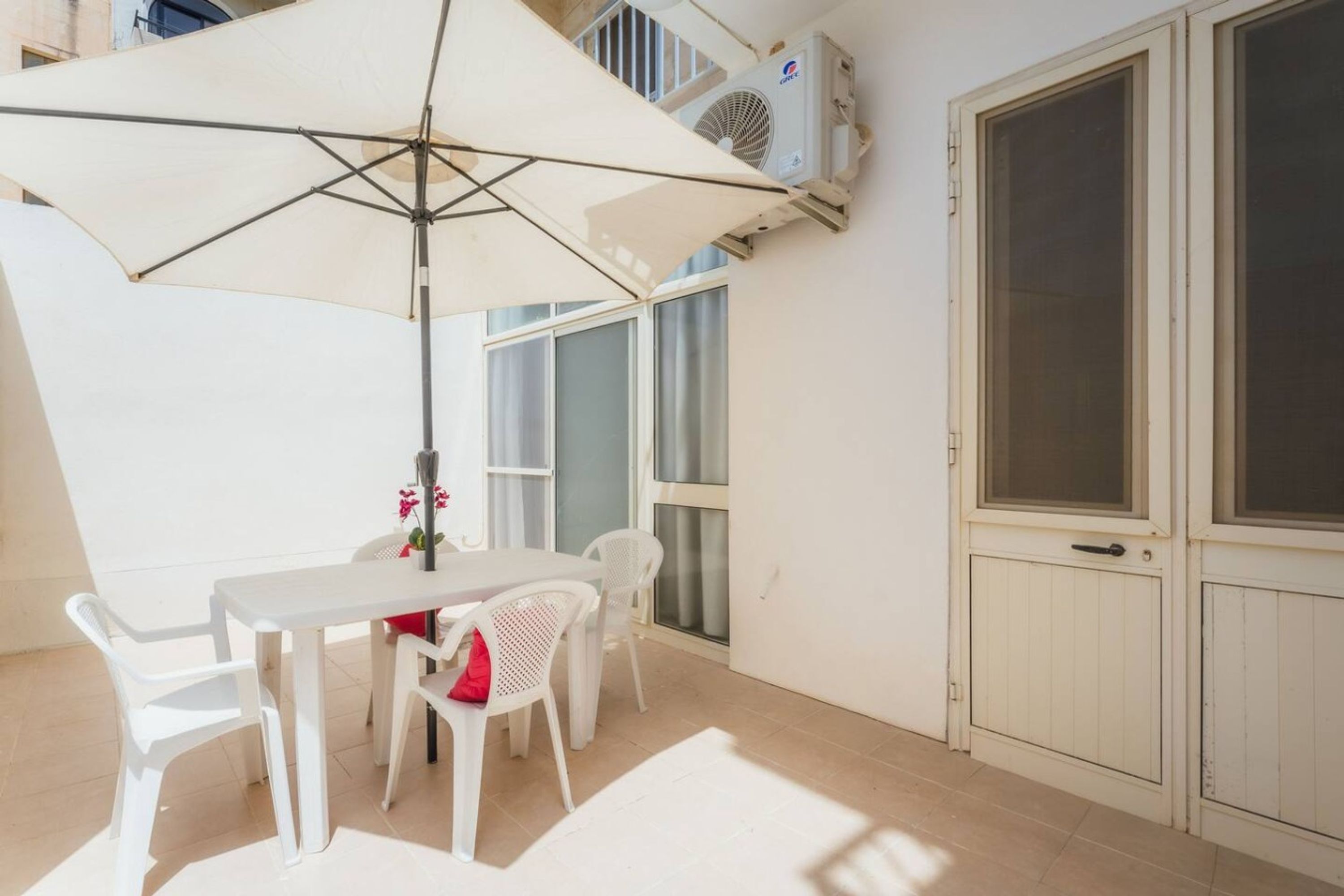 Un patio con una mesa, sillas, una sombrilla y un equipo de aire acondicionado.